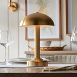 Endon Ashfield LED table lamp in brass with a domed shade and fluted stem, lit on a dining table beside wine glasses and framed pineapple art.