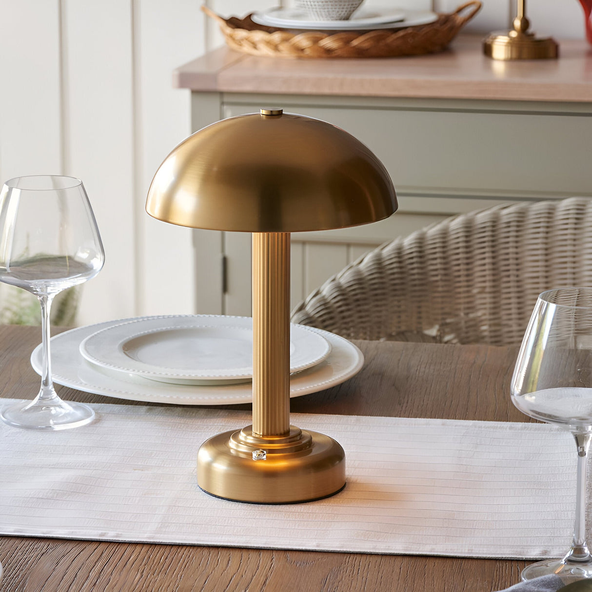 Endon Ashfield LED table lamp in brass with a domed shade and fluted stem, placed on a dining table with plates and wine glasses.