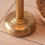 Close-up of the brushed brass fluted stem and rounded base of the Endon Ashfield LED table lamp on light wooden decking beside a wicker basket.