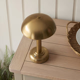 Endon Ashfield LED table lamp in brass with a domed shade and fluted stem, shown on a slatted wood table beside a wicker tray and fern.