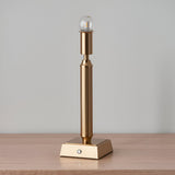 Endon Cranwick LED table lamp in brushed aged brass with reeded stem, square base, touch dimmer button, and clear globe bulb on a wooden surface.