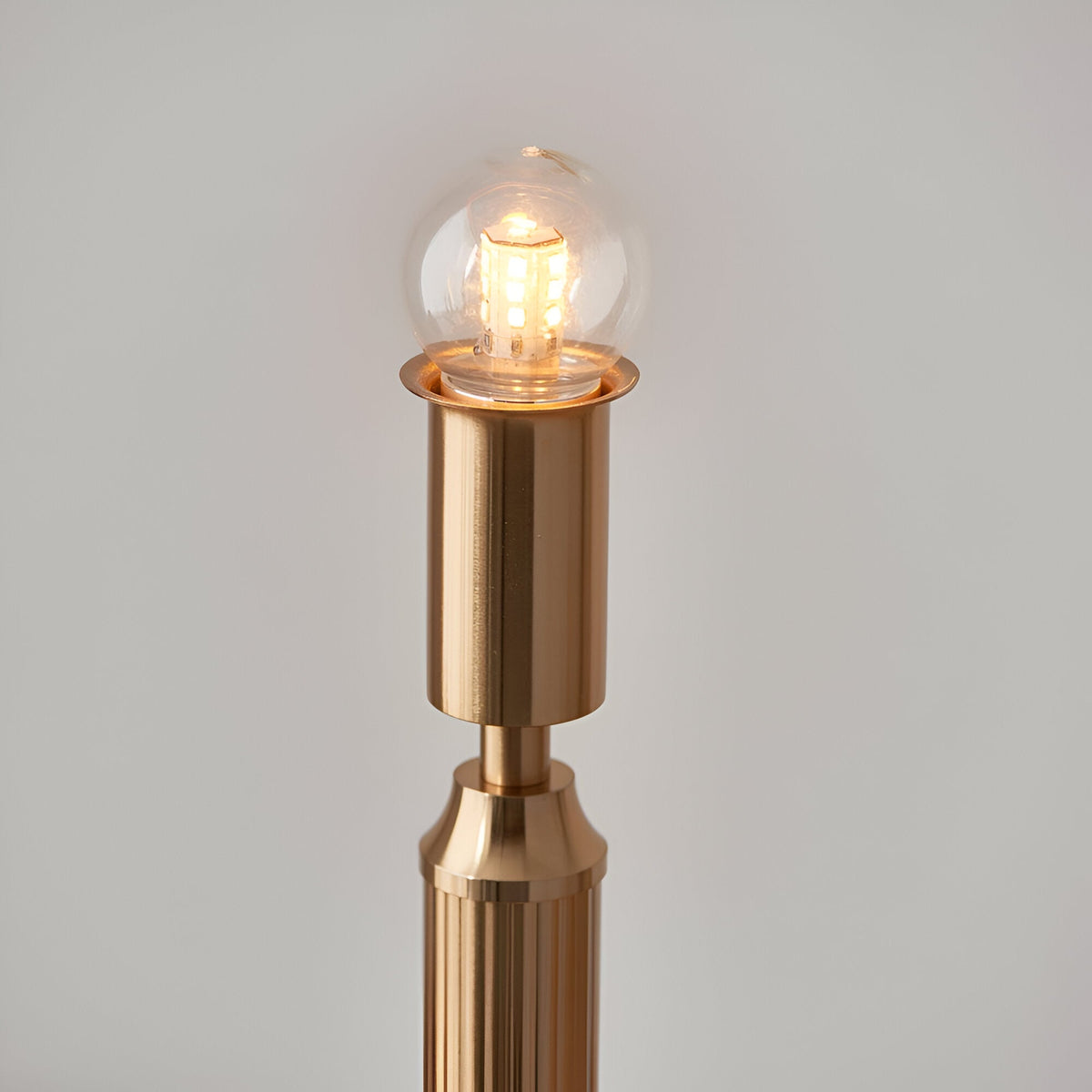 Close-up of the Endon Cranwick LED table lamp's brushed brass stem with lit integrated LED globe bulb, shown against a plain light background.