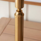 Close-up of the Endon Cranwick LED table lamp's brushed aged brass reeded stem rising from a square base on a light wooden surface.