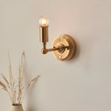 Endon Ashstead LED rechargeable wall light in brushed aged brass with a small clear globe bulb, mounted on a neutral wall beside dried grasses.