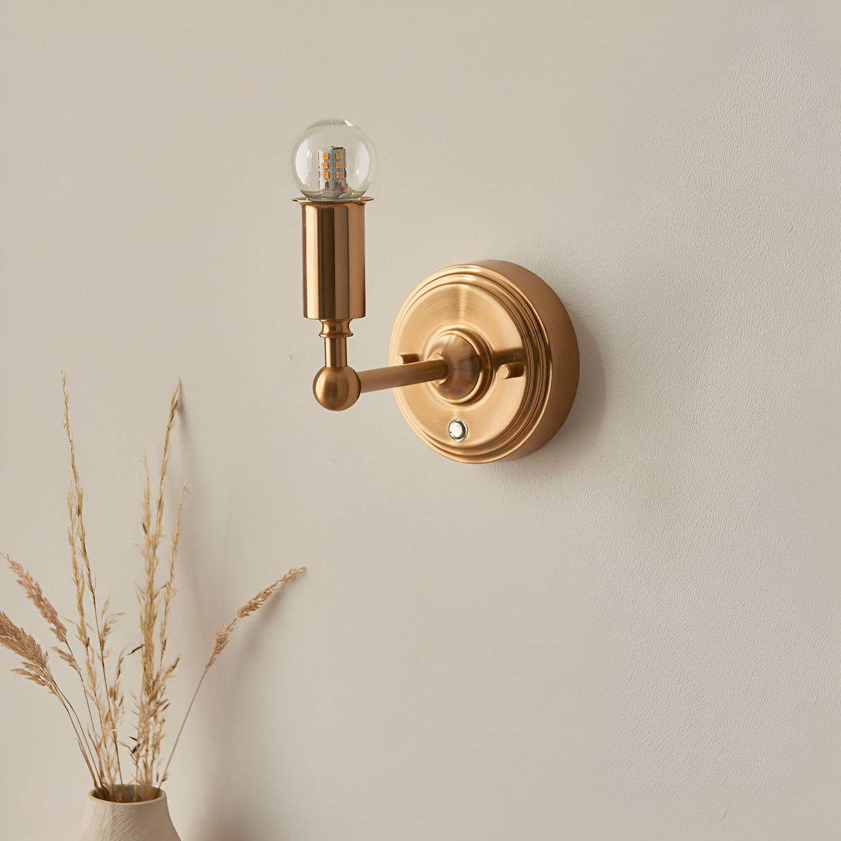Endon Ashstead rechargeable wall light in aged brass with a slim arm, exposed LED globe bulb, and round backplate, mounted on a neutral wall.