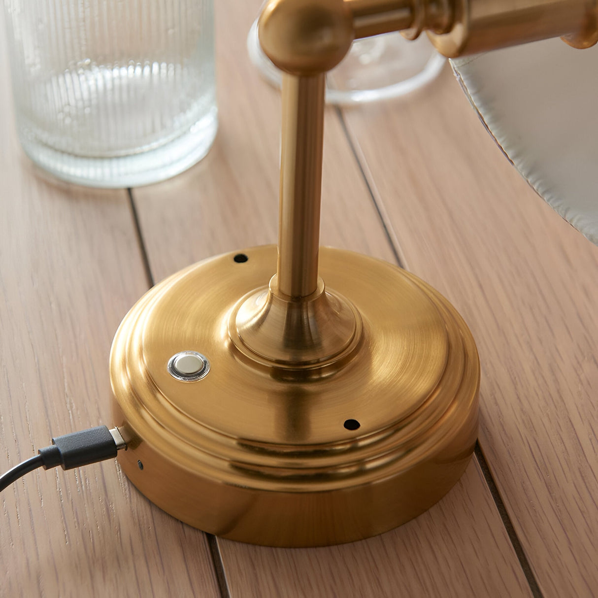 Close-up of the Endon Ashstead rechargeable wall light in brushed aged brass, showing the touch dimmer and connected USB-C charging cable on wood.