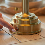 Danebourne LED Table Lamp in brushed antique brass, close-up of stepped base and touch dimmer button, finger pressing control on a wooden surface.