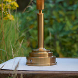 Danebourne LED Table Lamp base in brushed antique brass with stepped tiered design and touch dimmer button, shown outdoors on a table.