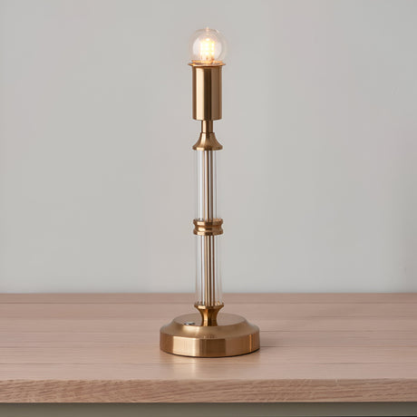 Endon Carlwood LED table lamp in brushed brass with clear acrylic detail and exposed globe bulb, shown on a wooden surface against a pale wall.