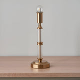 Endon Carlwood LED table lamp in brushed aged brass with clear acrylic column detail and exposed bulb, shown on a light wood surface.