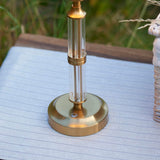 Endon Carlwood LED table lamp base in brushed aged brass with clear acrylic detailing and touch dimmer button, set on a striped cushion outdoors.