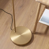 Close-up of the Endon Bevbourne floor lamp's round brushed brass base and stem on wood flooring, beside a wooden side table with a book.