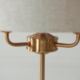 Close-up of the Brenley 3 Light Table Lamp in brass, showing three curved arms meeting a ribbed brass column beneath a linen shade.