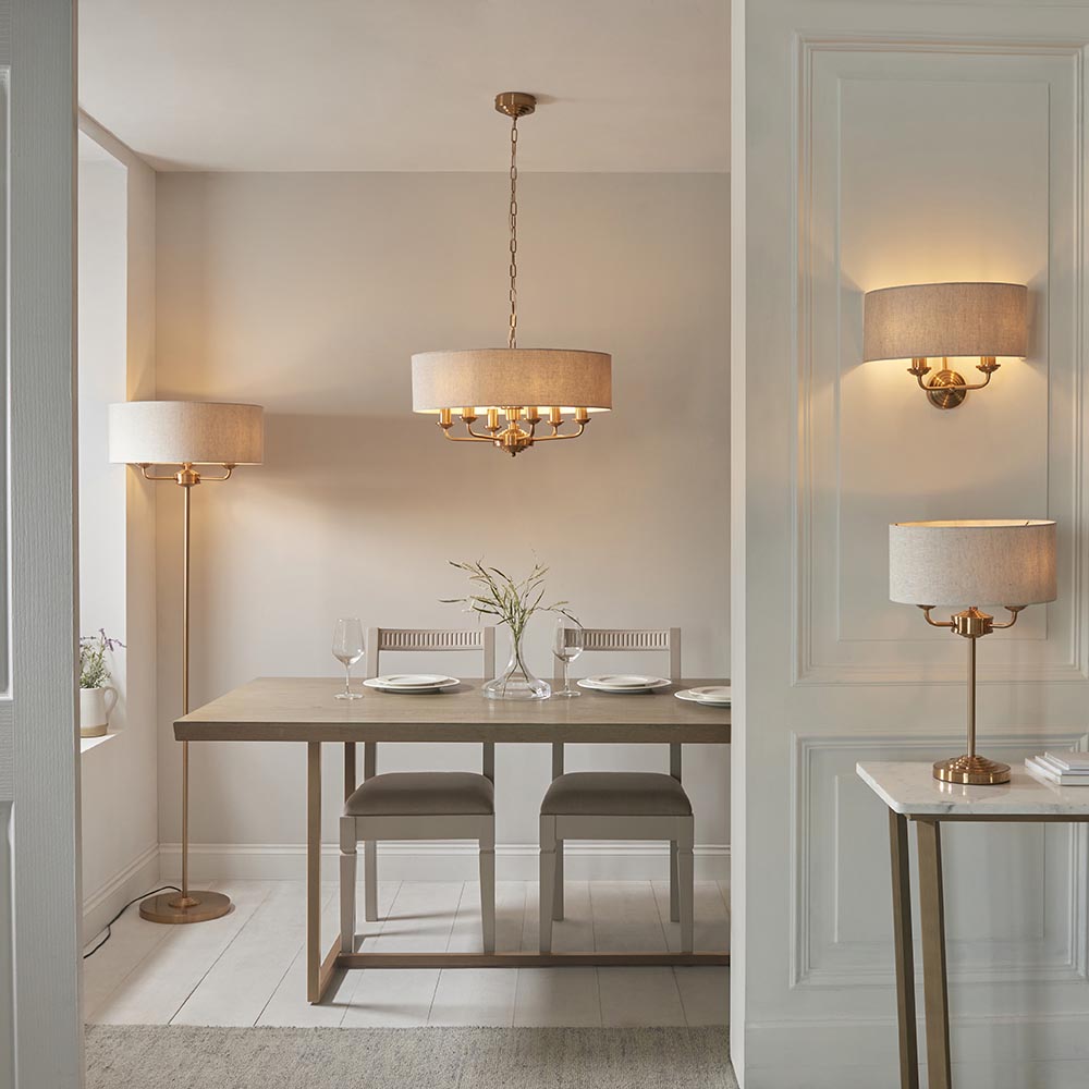 Brenley 3 Light Table Lamp in brass with a linen drum shade, shown on a marble-top console table beside a doorway in a dining room setting.