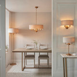Brenley 3 Light Table Lamp in brass with a linen drum shade, shown on a marble-top console table beside a doorway in a dining room setting.