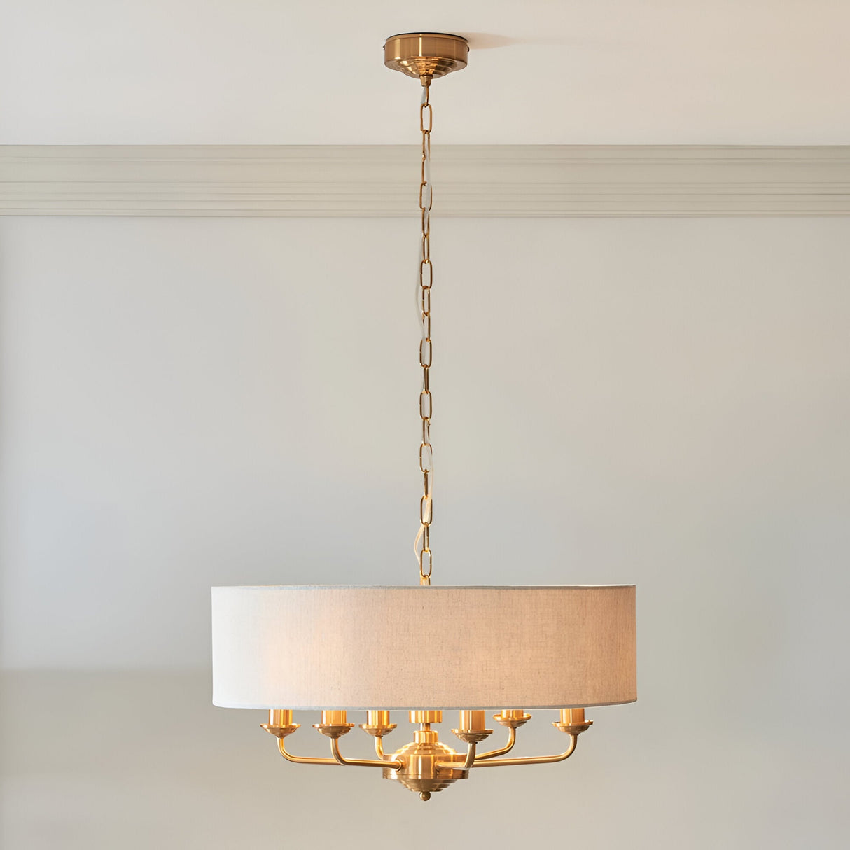 Endon Brenley 6 light pendant in vintage brass with a large natural linen drum shade, suspended by chain from a moulded ceiling in a neutral room.