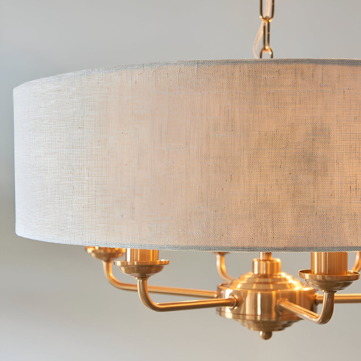 Close-up of Endon Brenley 6 Light Pendant in vintage brass with natural linen drum shade and hanging chain, showing E14 lamp holders on curved arms.
