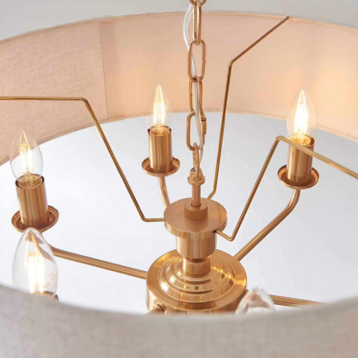 Close-up of Endon Brenley 6 Light Pendant in vintage brass, showing candle bulbs on angular arms beneath a natural linen drum shade.