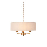 Brenley 3 Light Pendant in vintage brass with a natural linen drum shade, three exposed candle-style arms, and hanging chain, shown on a plain white background.