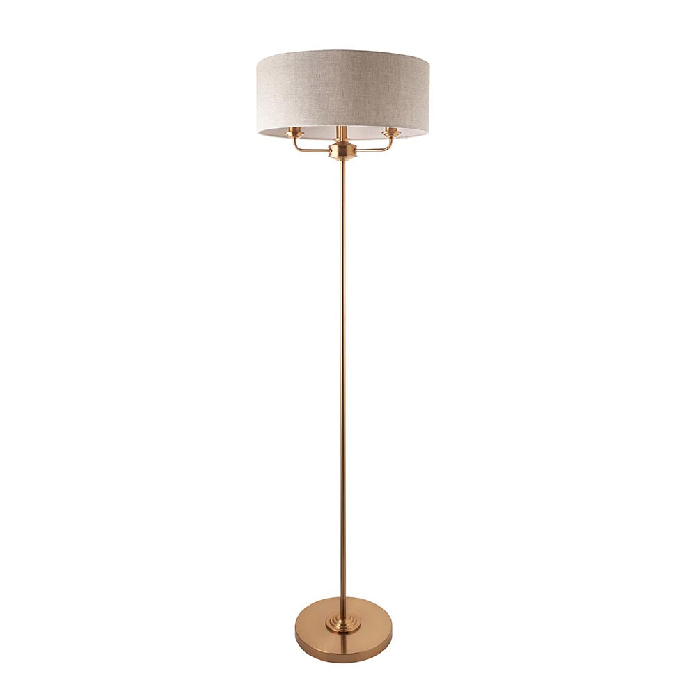 Endon Brenley 3 light floor lamp in vintage brass with a wide natural linen drum shade and round base, shown on a plain white background.