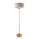 Endon Brenley 3 light floor lamp in vintage brass with a wide natural linen drum shade and round base, shown on a plain white background.