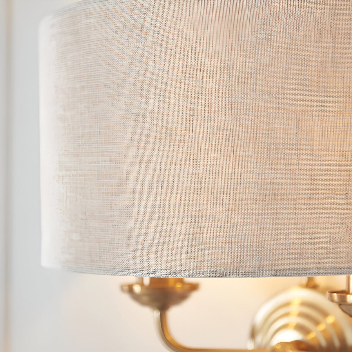 Close-up of the Endon Brenley 2 Light Wall Light showing the natural linen drum shade and vintage brass twin arms mounted to a pale wall.
