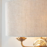 Close-up of the Endon Brenley 2 Light Wall Light showing the natural linen drum shade and vintage brass twin arms mounted to a pale wall.