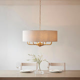 Endon Brenley pendant with wide natural linen drum shade on vintage brass frame, hanging above a dining table set with wine glasses and a vase.