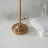 Close-up of Endon Brenley table lamp brass base, ridged circular design with slim stem, on a white marble surface beside stacked books.