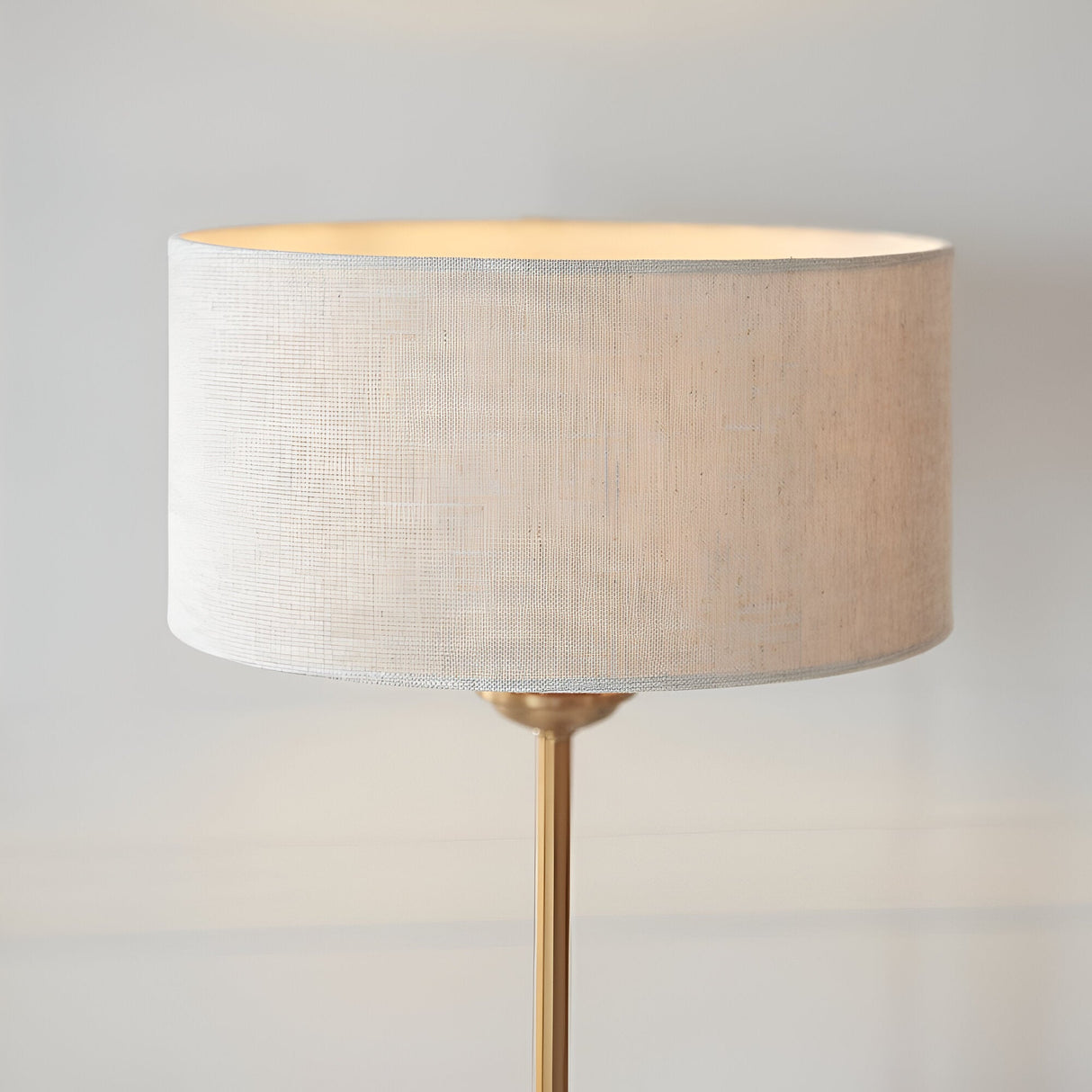 Endon Brenley table lamp with a natural linen drum shade and slim brass stem, shown lit against a plain light background.