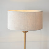 Endon Brenley table lamp with a natural linen drum shade and slim brass stem, shown lit against a plain light background.
