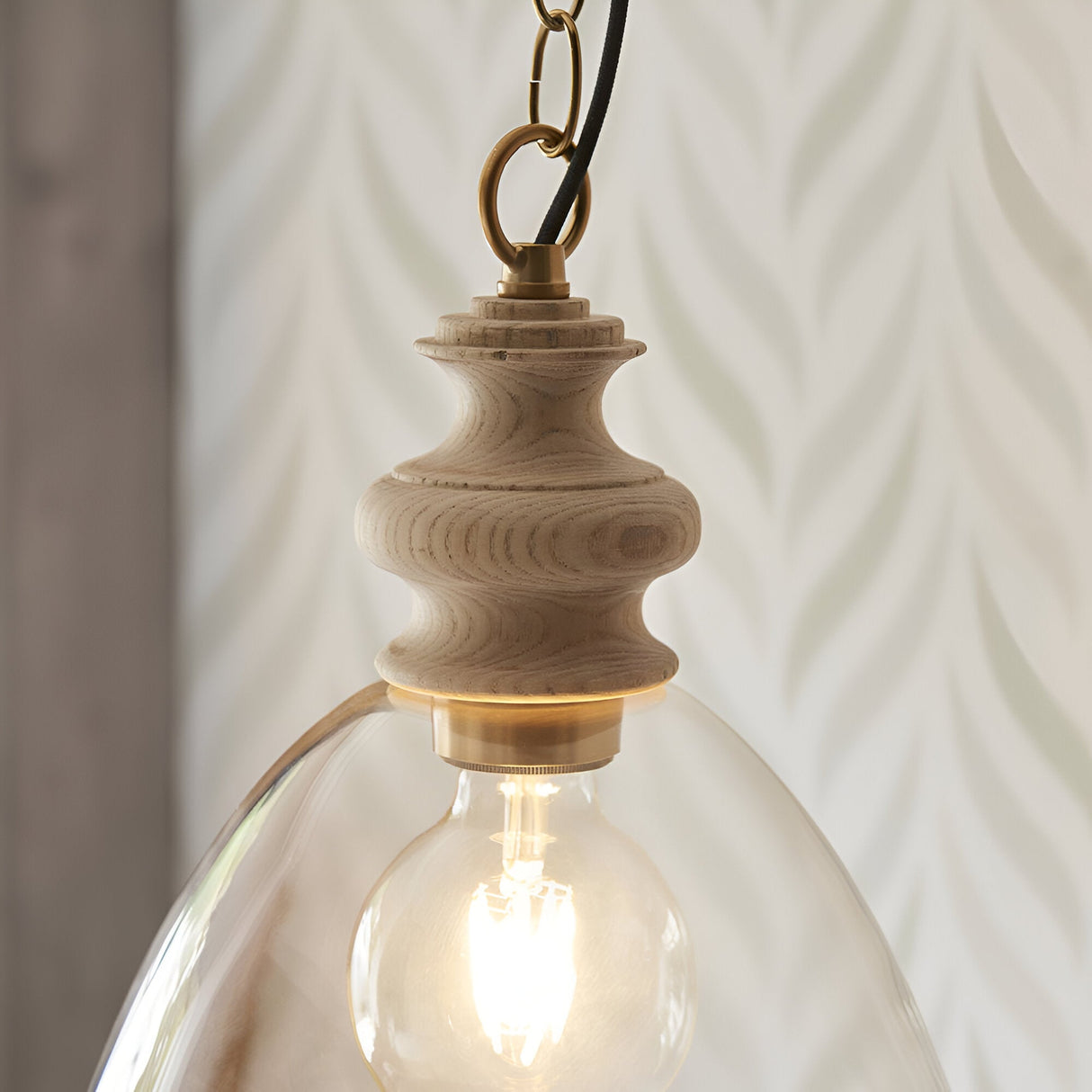 Bevwick Pendant close-up showing turned natural ash wood top, brushed brass fitting, black cable, and clear glass shade with visible E27 bulb.