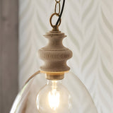 Bevwick Pendant close-up showing turned natural ash wood top, brushed brass fitting, black cable, and clear glass shade with visible E27 bulb.