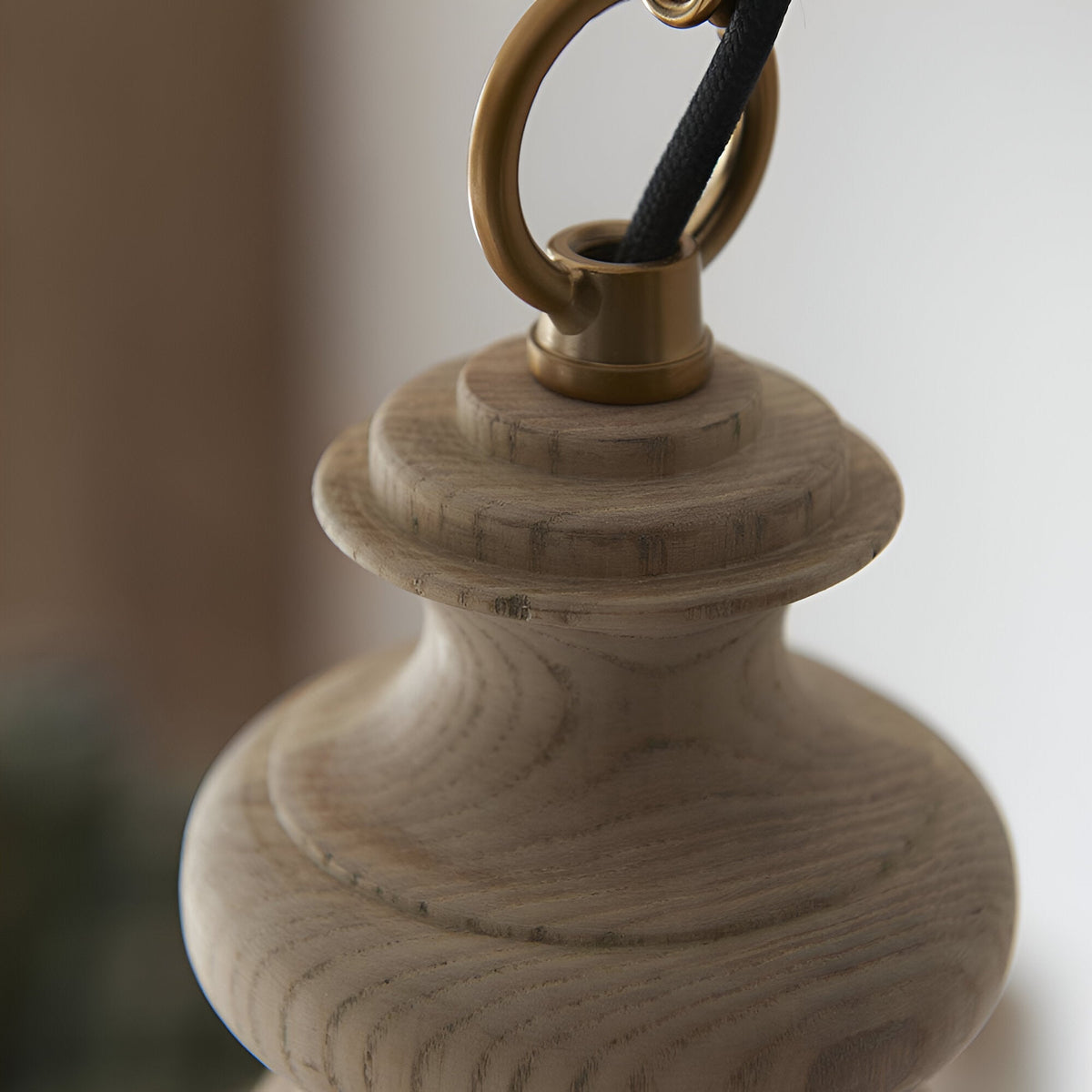 Close-up of the Bevwick pendant light's turned solid ash wood body with brushed antique brass hook and fabric flex cord against a neutral background.