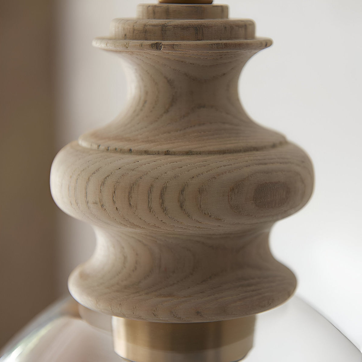 Bevwick pendant light close-up showing turned natural ash wood body with brushed brass banding above a clear flared glass shade, on a light background.