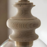 Bevwick pendant light close-up showing turned natural ash wood body with brushed brass banding above a clear flared glass shade, on a light background.