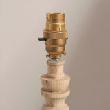 Close-up of the Endon Aldworth table lamp showing the brass B22 switched lampholder atop a turned natural wood spindle base against a neutral background.