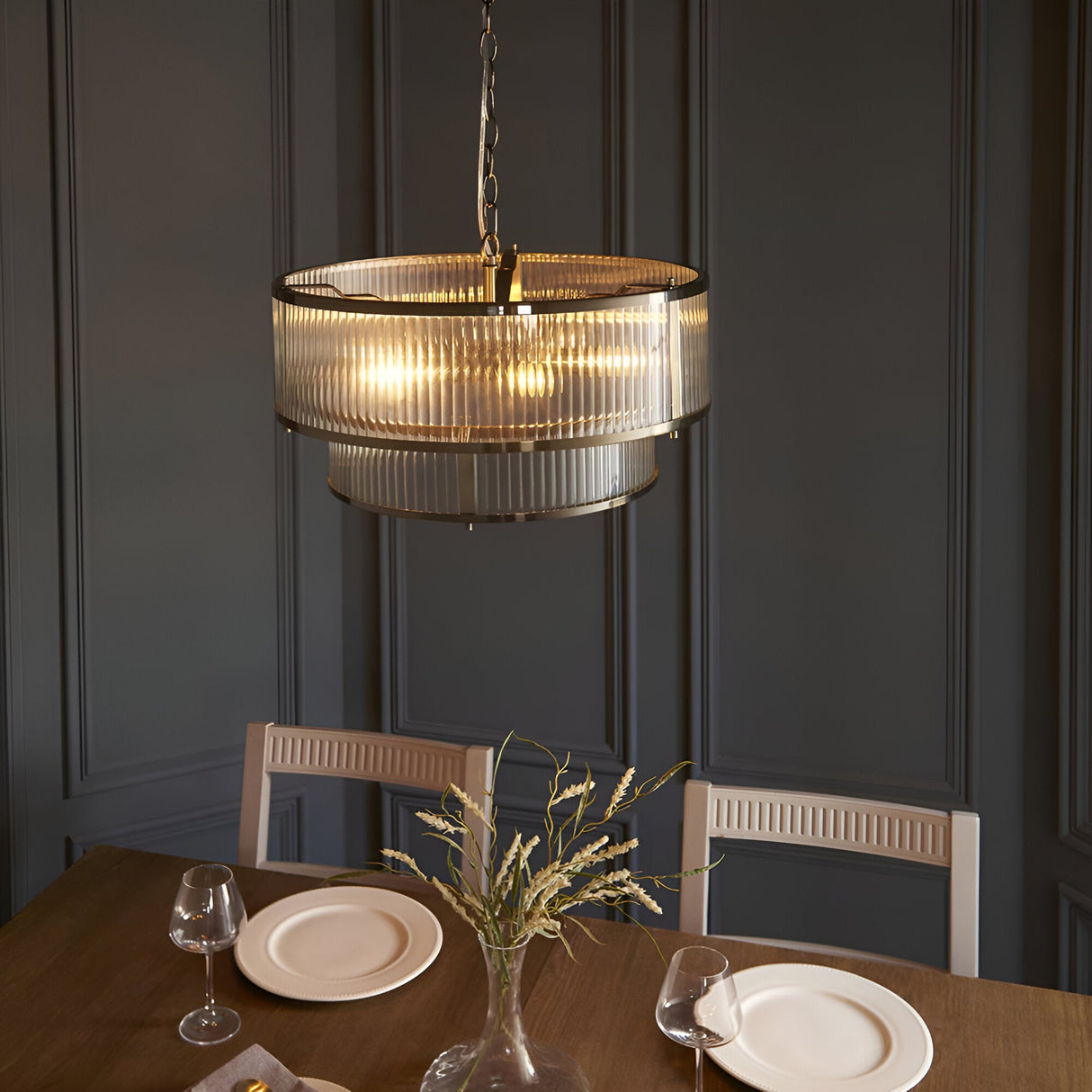 Endon Rothbury 5-light antique brass pendant with two tiers of clear ribbed glass shades, chain-hung above a dining table against panelled grey walls.