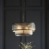 Endon Rothbury 5 light pendant in antique brass with two tiers of clear ribbed glass shades, suspended by chain against a dark panelled wall.