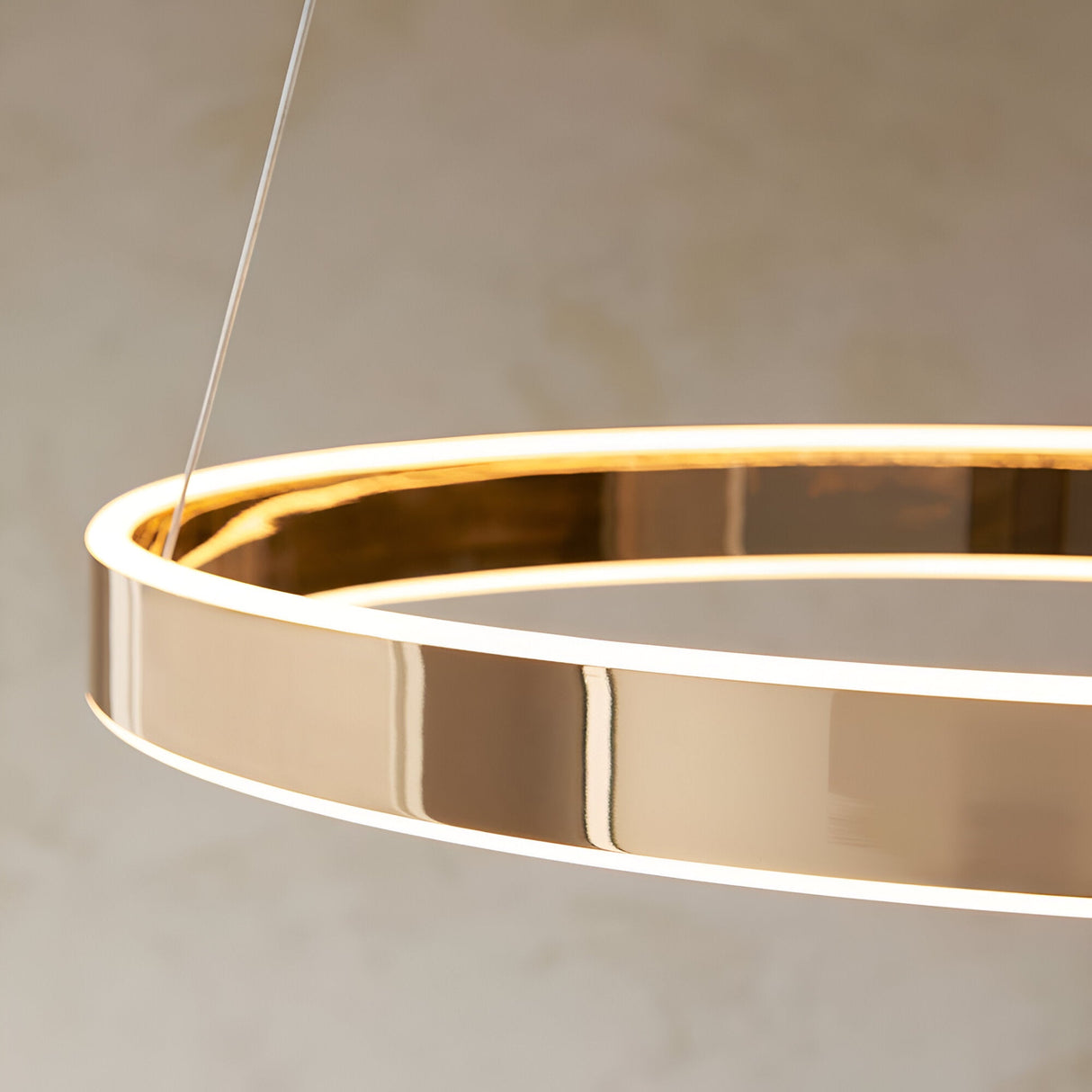 Close-up of the Endon Bramford LED pendant showing its slim gold ring fitting with frosted diffuser, suspended from fine wire cables against a neutral wall.