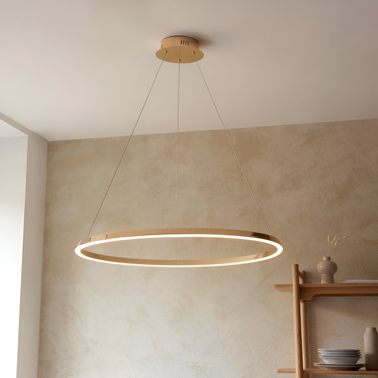 Cliffton LED pendant light with a slim circular gold-finish ring and white diffuser, suspended on fine cables above a dining area with wooden shelving.