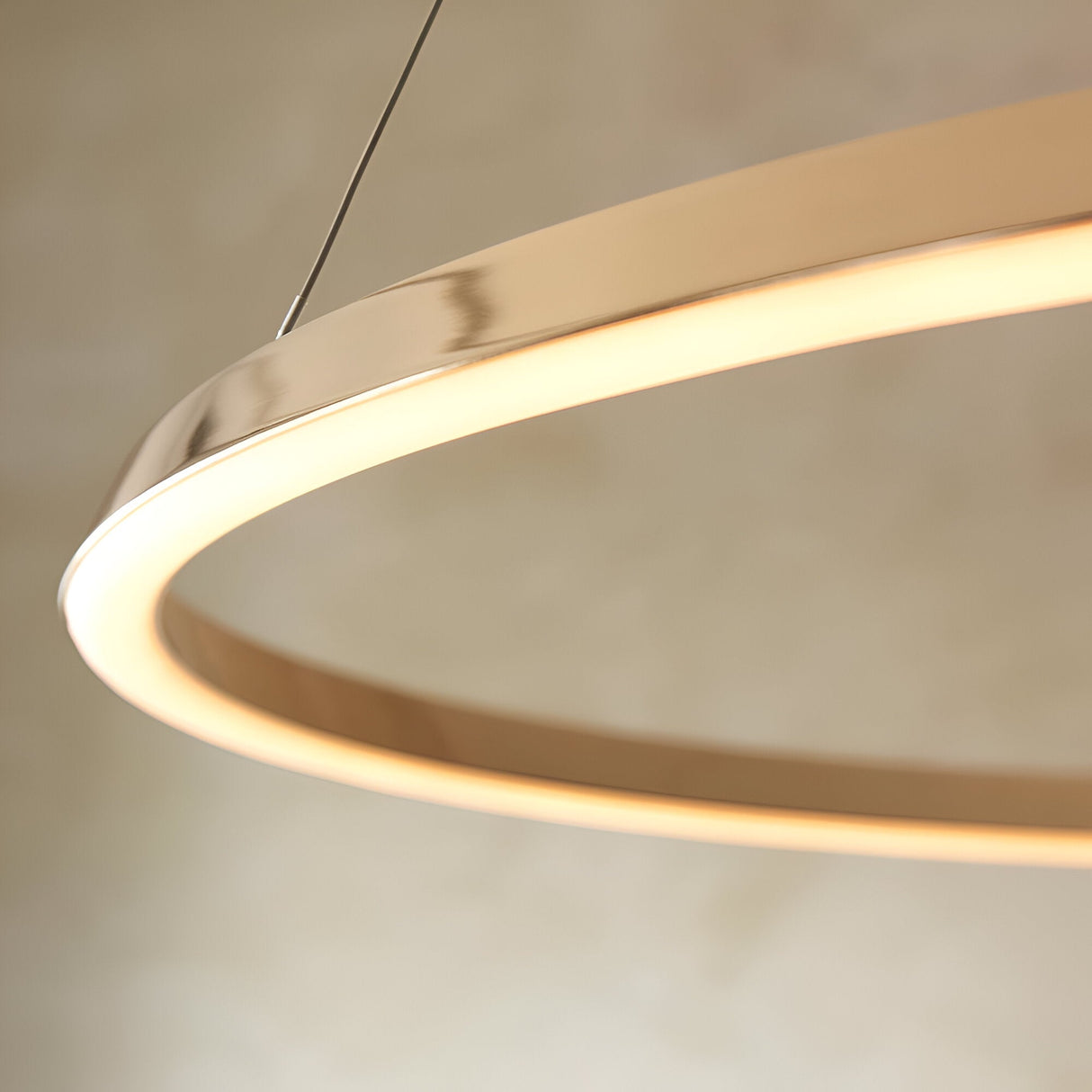 Close-up of the Cliffton LED pendant's circular gold metal ring with white diffuser edge, emitting warm white light, suspended by fine cables.