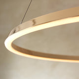 Close-up of the Cliffton LED pendant's circular gold metal ring with white diffuser edge, emitting warm white light, suspended by fine cables.
