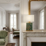 Elegant living room with ornate white walls, a gold-framed mirror above a marble fireplace, and the Veridan 1 Light Framed Marble Table Lamp in brass & green. Green furniture and large windows with beige curtains add sophistication.