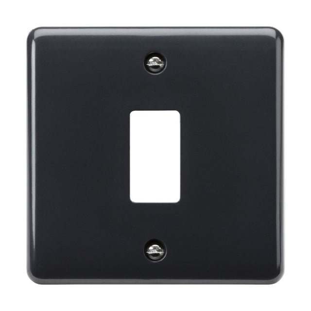 A black 1 Gang Grid Faceplate with a curved edge and a central cutout for a single toggle switch. It includes two visible screws, one at the top and one at the bottom, securing it in place. Designed to meet British Safety standards, this faceplate offers both style and safety as part of the Part M compliant range.