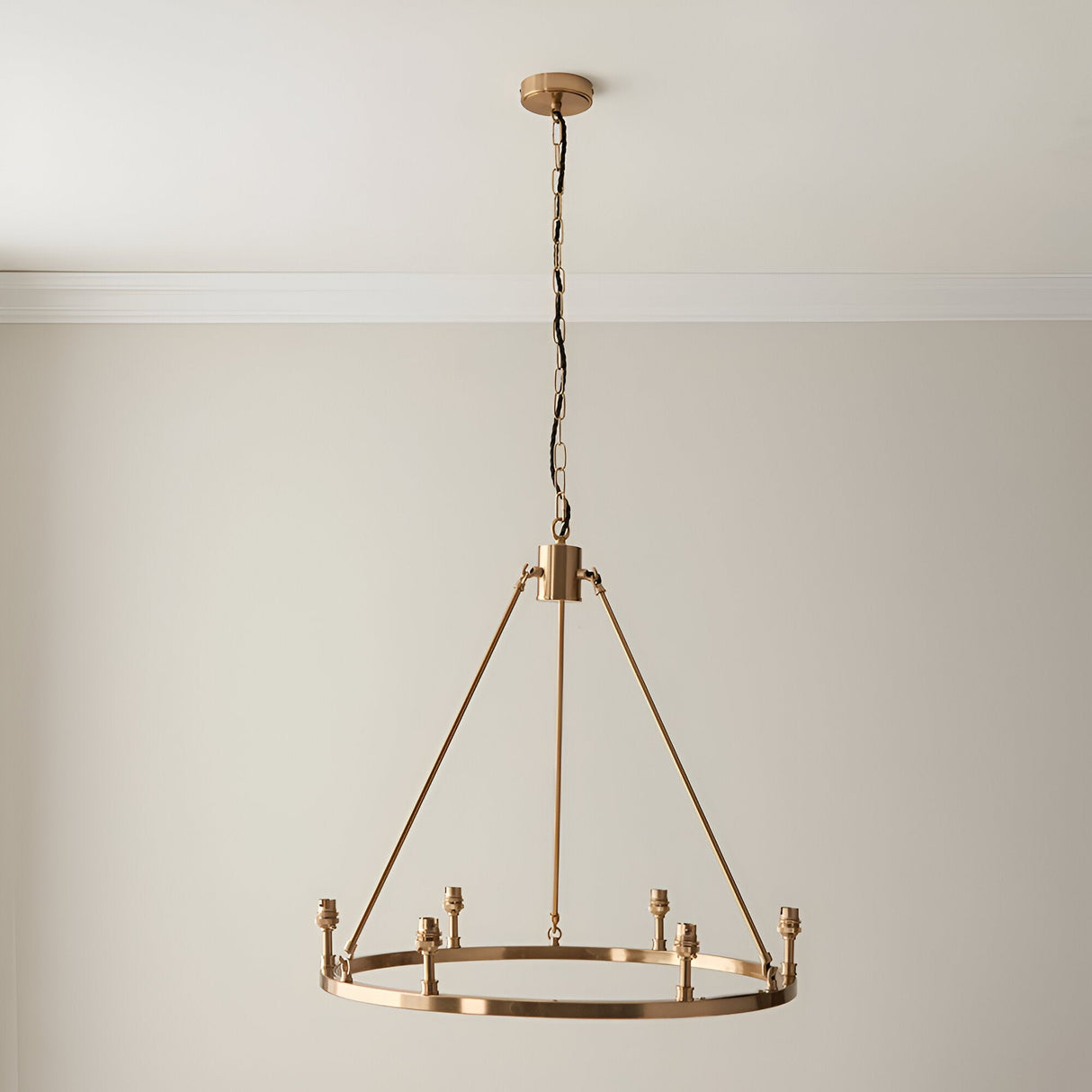 Endon Bevford 6 light hoop pendant in aged brass with six B22 lamp holders, suspended from a chain with black fabric flex against a pale wall.
