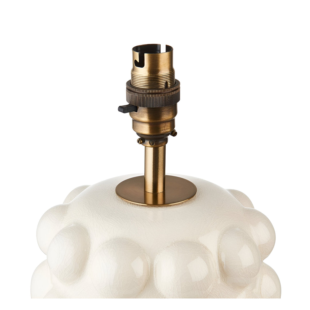 Amberley table lamp base close-up showing aged brass B22 lamp holder with switch on a white ceramic bobble-textured base, plain background.
