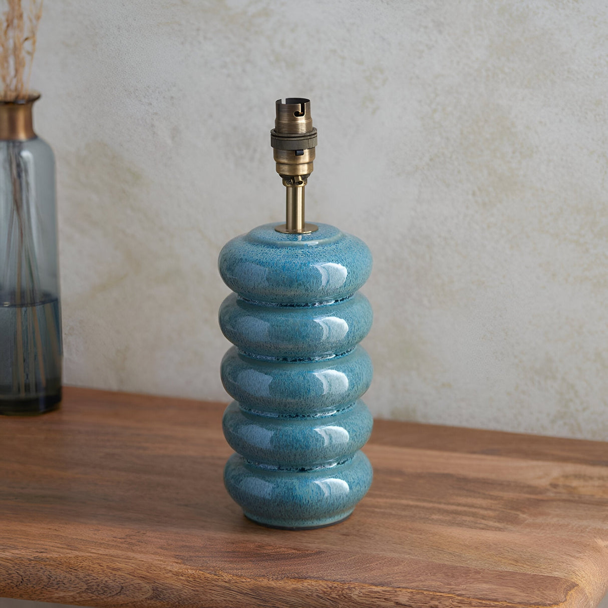 Cliffstead Table Lamp base in ceramic with ribbed curves and blue reactive glaze, brushed aged brass B22 holder, shown on a wooden surface.