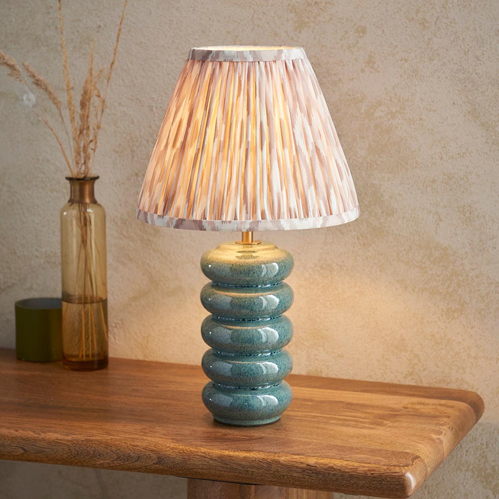 Cliffstead Table Lamp with ribbed teal reactive-glaze ceramic base and pleated pink patterned shade, shown on a wooden table beside a glass vase.