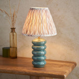 Cliffstead Table Lamp with ribbed teal reactive-glaze ceramic base and pleated pink patterned shade, shown on a wooden table beside a glass vase.